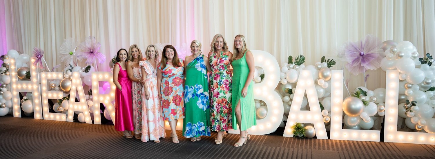 Group pf women standing in front of large lighted letters spelling out Heart Ball.
